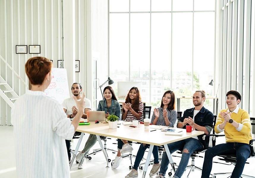 Businesswoman explain ideas to group of creative diverse team at Businesswoman explain ideas to group of creative diverse team at modern office. Rear view of manager gesturing hand standing against multiethnic people. Audience applauding speaker after presentation.