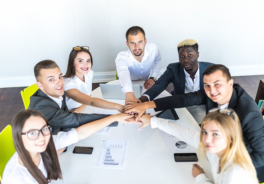 Unity concept. Close-up of multi ethnic people holding hands together while sitting around the desk Unity concept. Close-up of people holding hands together while sitting around the desk